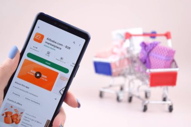 Kharkiv, Ukrayna, 31 Mart 2023: Akıllı telefonlu alışveriş arabası pembe arka planda Alibaba logosu açtı.