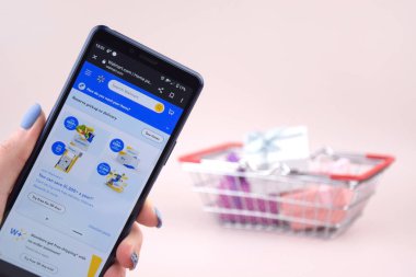 Kharkiv, Ukrayna, 31 Mart 2023: Akıllı telefonlu alışveriş arabası mavi arka planda Walmart logosu açtı.