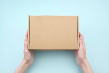Kadın eli, doğal kıvrımlı kartondan yapılmış kahverengi ekolojik paket kutusunu tutuyor. Paketleme, alışveriş, teslimat konsepti.