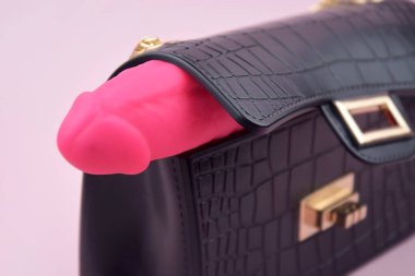 Pink dildo in a small black purse on a light background with copyspace text for a sex shop. The concept of sexual health.