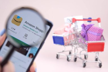 KHARKOV, UKRAINE - Mart 31,2023: Akıllı telefonlu alışveriş arabası ekranda pembe arka planda Amazon logosu açtı. Amazon - Uluslararası Elektronik Ticaret Şirketi.