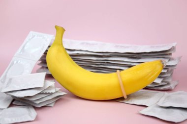 Pembe arka planda kondom ve muz. Cinsel sağlık kavramı.