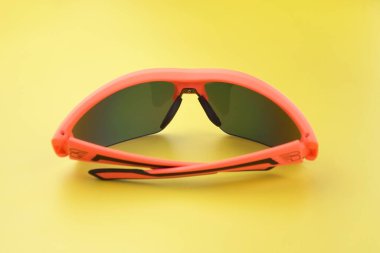 Sarı lensli turuncu plastikten yapılmış spor gözlükleri, sarı arka planda çekiliyor..