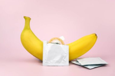 Pembe arka planda kondom ve muz. Cinsel sağlık kavramı.