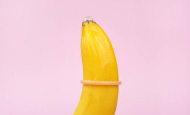 Pembe arka planda kondom ve muz. Cinsel sağlık kavramı.