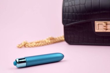 A blue bullet-dildo in a small black purse on a light background with copyspace text for a sex shop. The concept of sexual health.