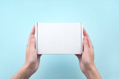 Mavi arka planda beyaz paket kutusunu tutan kadın eller. Paketleme, alışveriş, teslimat konsepti.