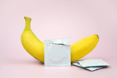 Pembe arka planda kondom ve muz. Cinsel sağlık kavramı.