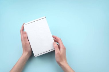 Mavi arka planda beyaz paket kutusunu tutan kadın eller. Paketleme, alışveriş, teslimat konsepti.