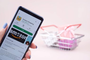 KHARKOV, UKRAINE - Mart 31,2023: Akıllı telefonlu alışveriş arabası ekranda pembe arka planda Amazon logosu açtı. Amazon - Uluslararası Elektronik Ticaret Şirketi.