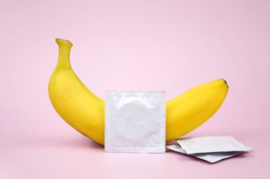 Pembe arka planda kondom ve muz. Cinsel sağlık kavramı.