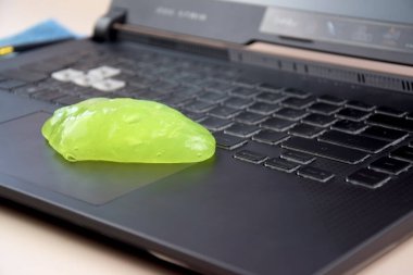 Kharkiv, Ukrayna, 11 Temmuz 2023: Laptop klavyesindeki tozları temizlemek için yeşil yumuşak temizlik jeli Asus Rog Strix. Bilgisayar klavyeni temizleme konsepti. Ofis temizliği.