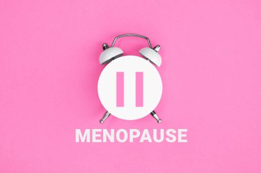Pembe zemin üzerinde MENOPAUSE yazan beyaz antika alarm saati. Kadın Sağlığı. Düz yatıyordu.
