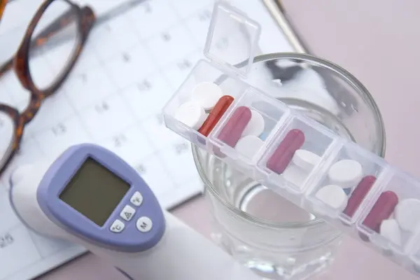 Calendar with pills and non-contact thermometer. The concept of treatment from diseases.