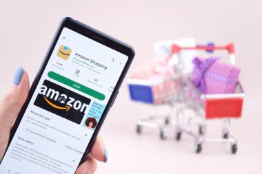 KHARKOV, UKRAINE - Mart 31,2023: Akıllı telefonlu alışveriş arabası ekranda pembe arka planda Amazon logosu açtı. Amazon - Uluslararası Elektronik Ticaret Şirketi.