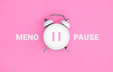 White vintage alarm clock with an inscription MENOPAUSE on pink background. Women Health. Flat lay. clipart