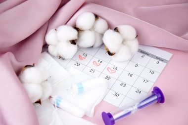 Kadınların adet pedleri, tamponlar, adet takvimi ve pembe arka planda çalar saat. Kritik Günlerin Süresi.