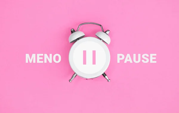 stock image White vintage alarm clock with an inscription MENOPAUSE on pink background. Women Health. Flat lay.