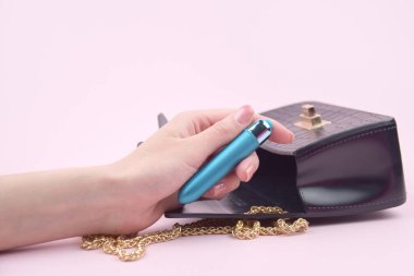 A blue bullet-dildo in a small black purse on a light background with copyspace text for a sex shop. The concept of sexual health.