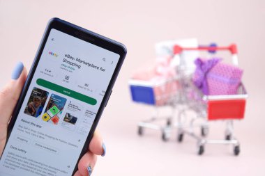 Kharkiv, Ukrayna, 31 Mart 2023: Akıllı telefonlu alışveriş arabası pembe arka planda Ebay uygulamasını açtı.
