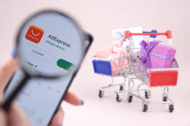Kharkiv, Ukrayna, 31 Mart 2023: Akıllı telefonlu alışveriş arabası pembe arka planda Aliexpress logosu açtı.