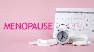 Pembe zemin üzerinde MENOPAUSE yazan beyaz antika alarm saati. Kadın Sağlığı.