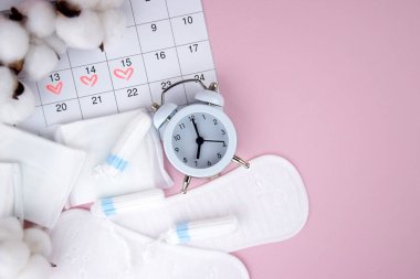 Kadınların adet pedleri, tamponlar, adet takvimi ve pembe arka planda çalar saat. Kritik günler dönemi. Metin için yer.