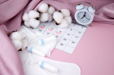 Kadınların adet pedleri, tamponlar, adet takvimi ve pembe arka planda çalar saat. Kritik günler dönemi. Metin için yer.