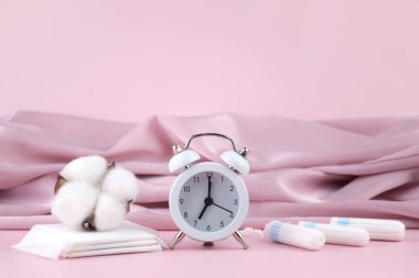 Kadınların adet pedleri, tamponlar, adet takvimi ve pembe arka planda çalar saat. Kritik günler dönemi. Metin için yer.