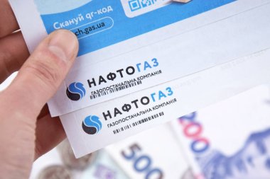 KHARKIV, UKRAINE - MARCH 2, 2024: Receipt for utility services of Naftogaz with money in Ukrainian hryvnias on the light table. clipart