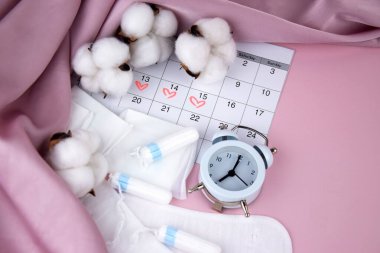 Kadınların adet pedleri, tamponlar, adet takvimi ve pembe arka planda çalar saat. Kritik günler dönemi. Metin için yer.