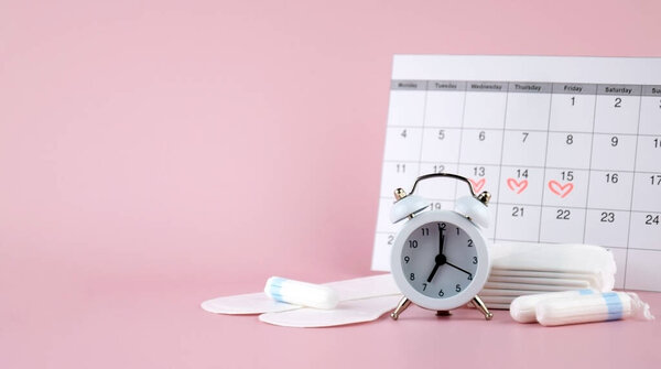 Женские менструальные прокладки, тампоны, женский календарь менструации и будильник на розовом фоне. Период критических дней. Место для текста.