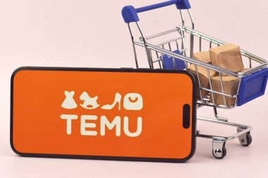 KHARKOV, UKRAINE - 18 Ağustos 2024: Akıllı telefonlu alışveriş arabası turuncu arka planda TEMU uygulaması açık.