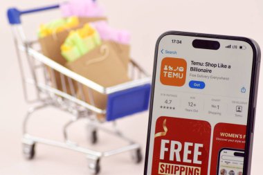 KHARKOV, UKRAINE - 18 Ağustos 2024: Akıllı telefonlu alışveriş arabası turuncu arka planda TEMU uygulaması açık.