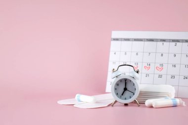 Kadınların adet pedleri, tamponlar, adet takvimi ve pembe arka planda çalar saat. Kritik günler dönemi. Metin için yer.