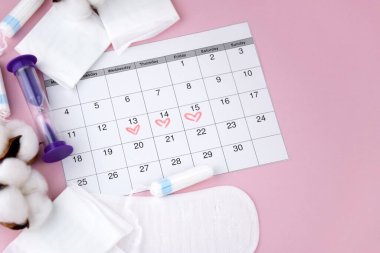 Kadınların adet pedleri, tamponlar, adet takvimi ve pembe arka planda çalar saat. Kritik günler dönemi. Metin için yer.