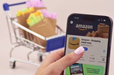 KHARKOV, UKRAINE - 18 Ağustos 2024: Akıllı telefonlu alışveriş arabası beyaz arka planda Amazon açık.