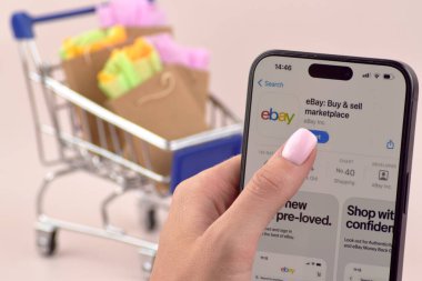 KHARKOV, UKRAINE - 18 Ağustos 2024: Akıllı telefonlu alışveriş arabası ekranda Ebay uygulaması açık.