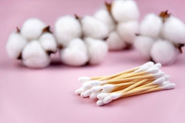 Kulak çubukları, pembe arka planda beyaz pamuk pedler. Vücut hijyeni ve kişisel bakım kavramını.