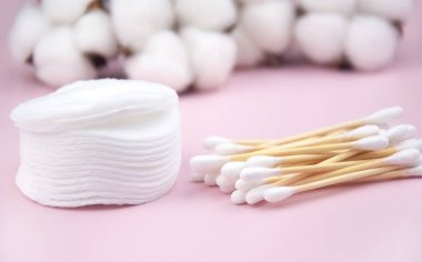 Kulak çubukları, pembe arka planda beyaz pamuk pedler. Vücut hijyeni ve kişisel bakım kavramını.