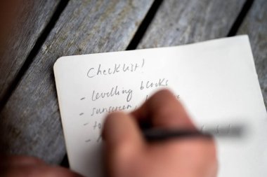 gril writing a camping list in a piece of paper. writing a check list with a pencil in australia