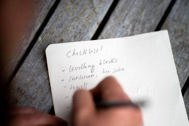 gril writing a camping list in a piece of paper. writing a check list with a pencil in australia