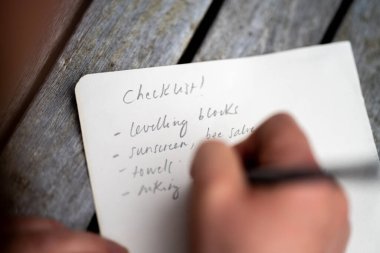 gril writing a camping list in a piece of paper. writing a check list with a pencil in australia