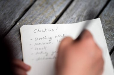 gril writing a camping list in a piece of paper. writing a check list with a pencil in australia