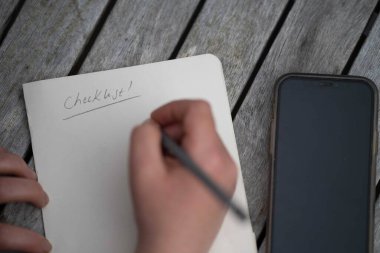 gril writing a camping list in a piece of paper. writing a check list with a pencil in australia