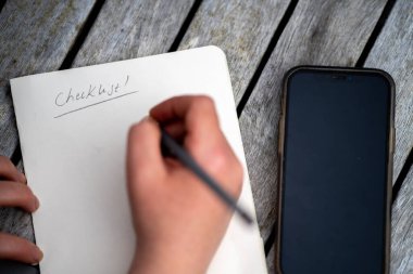 gril writing a camping list in a piece of paper. writing a check list with a pencil in australia