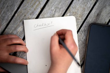 gril writing a camping list in a piece of paper. writing a check list with a pencil in australia