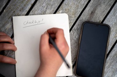 gril writing a camping list in a piece of paper. writing a check list with a pencil in australia