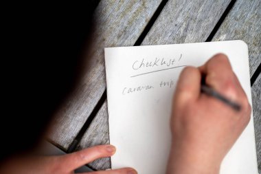 gril writing a camping list in a piece of paper. writing a check list with a pencil in australia