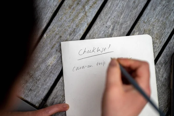 gril writing a camping list in a piece of paper. writing a check list with a pencil in australia